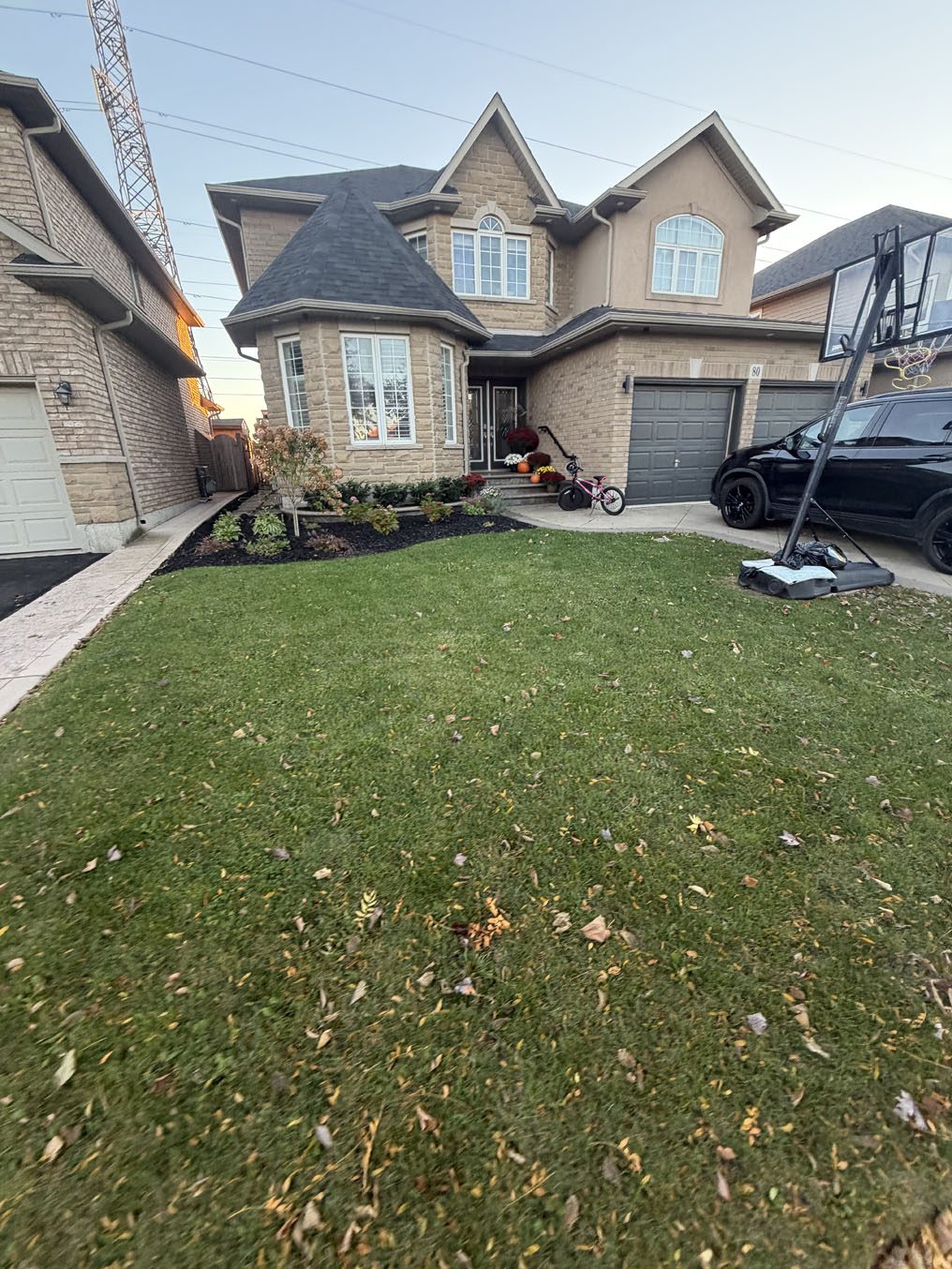 Green lawn beside freshly mulched garden beds at a turret-style home in Hamilton