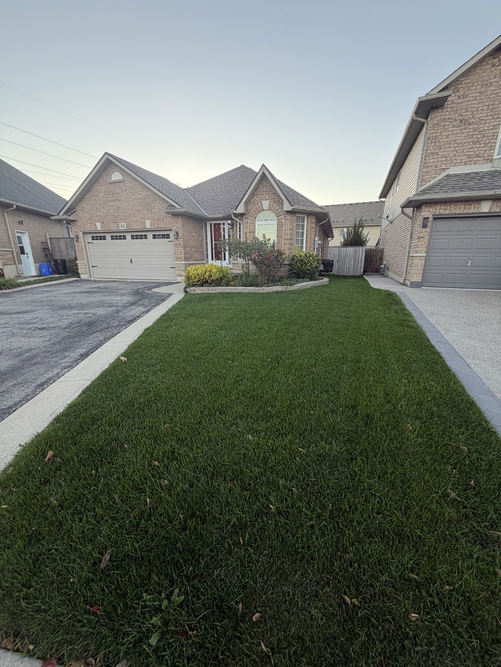 Narrow striped sod lawn between two driveways leading to a Hamilton bungalow